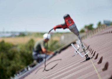 Close up of clamp. Worker prepearing to installation photovoltaic solar panel system on the roof of house. Man and electric screwdriver on blurred background.