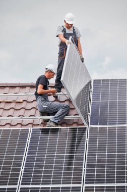 Men technicians mounting photovoltaic solar moduls on roof of house. Engineers in helmets installing solar panel system outdoors. Concept of alternative and renewable energy.