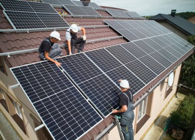 Men installers mounting photovoltaic solar moduls on roof of house. Engineers in helmets installing solar panel system outdoors. Concept of alternative and renewable energy. Aerial view.