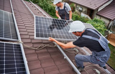 Men technicians carrying photovoltaic solar moduls on roof of house. Engineers in helmets building solar panel system outdoors. Concept of alternative and renewable energy.