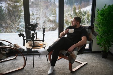 Kameraman koltukta dinleniyor, kamerasının yanında çay içiyor. Dengeleyici ekipmanına monte edilmiş..