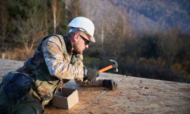 Marangoz, gelecekteki kulübenin çatısında OSB paneline çivi çakıyor. Ahşap çerçeve inşa eden bir işçi. Marangozluk ve inşaat konsepti.