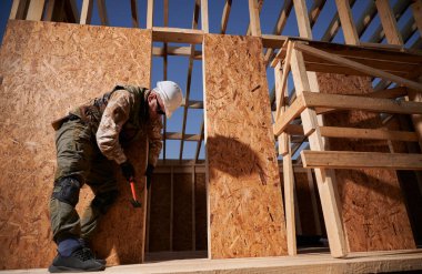 Marangoz, OSB panelinin duvarına çivi çakıyor. Ahşap çerçeve inşa eden bir işçi. Marangozluk ve inşaat konsepti.