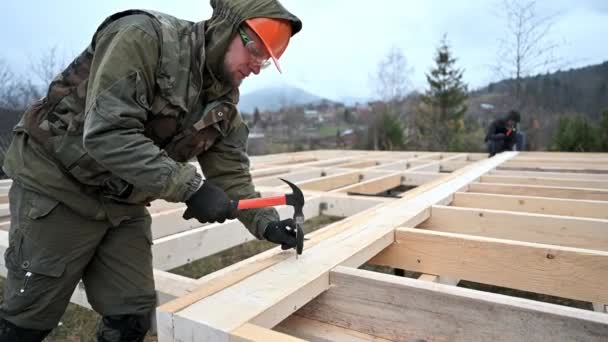 杭基礎の上に木造フレームハウスを構築男労働者 ハンマーを使用して 木製のジョイストにカーペンターハンマー爪 大工の概念 — ストック動画