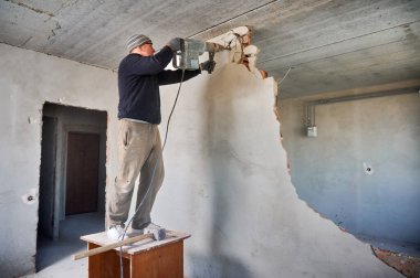 İşçi evin içindeki küçük masada duruyor ve duvarları sökmeye devam ediyor. Performanslı bir inşaatçı, bölmenin üst kısmını tavana yakın bir yerde yok ediyor..