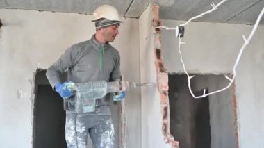 İşyeri inşaatçısının çekiç matkapla sondaj duvarını yan görüntüsü. Erkek işçi, tadilat altındaki dairedeki duvarı yıkarken matkap kullanıyor. Yıkım işleri ve ev yenileme konsepti.
