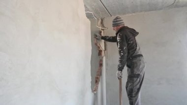 Ahşap masanın üzerinde duran ve ev tadilatı yaparken çekiçle duvarı kıran adam. Balyoz tutan erkek işçi, tadilat altındaki odada duvarları yıkıyor..