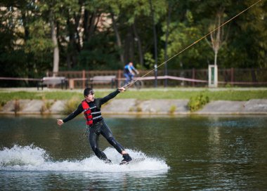 Wakeboardcu gölde sörf yapıyor. Genç sörfçü kablo parkında sörf yaparken eğleniyor. Su sporu, açık hava aktivitesi konsepti.