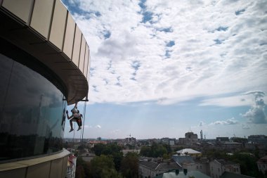 Endüstriyel dağcılık çamaşır makinesi ipe tutunuyor ve gökdelenlerin camlarını temizliyor. Yüksek binaların camlarını silerken güvenlik kaldırma ekipmanı kullanan erkek woker.