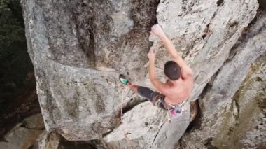 Genç adam halatla yüksek bir kayanın üzerinde zor bir yola tırmanıyor. Korkusuz dağcı yaz günü kaya tırmanışı eğitimi alıyor. Ekstrem spor, macera ve aktif yaşam tarzı kavramı. Hava görünümü.
