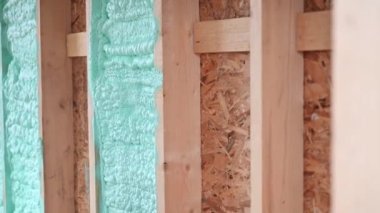 Erkek müteahhit ahşap iskeleti yalıtıyor. Adam işçi, gelecekteki kulübenin içine poliüretan köpük püskürtüyor, çoğul bileşen silah kullanıyor. İnşaat ve yalıtım konsepti.