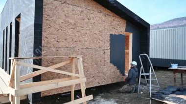 Boya silindiri kullanan erkek ressam, dış boyayı siyah renkte yapıyor. Ahşap çerçeve inşa eden bir işçi. Marangozluk ve inşaat konsepti.