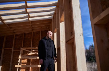 Erkek mühendis ahşap çerçeve inşa ediyor. İnşaat alanında duran kel adam güneşli bir günde iş kalitesini kontrol ediyor..