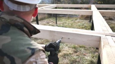 Ahşap çerçeve inşa eden adam. Gelecekteki kulübelerin ahşap çerçevesinde elektrikli matkapla delik açan işçiler. Marangozluk kavramı.