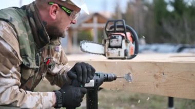 Ahşap çerçeve inşa eden adam. Gelecekteki kulübelerin ahşap çerçevesinde elektrikli matkapla delik açan işçiler. Marangozluk kavramı.