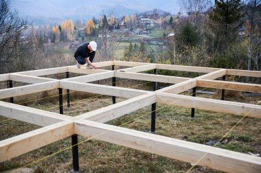 Yığınla temele ahşap çerçeve inşa eden bir işçi. Marangoz ahşap kalasları ölçüyor ve kurşun kalemle iz bırakıyor. Marangozluk kavramı.