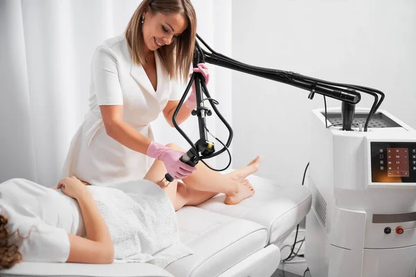 皮肤科医生与现代激光设备一起致力于皮肤缺陷的抛光和修复 美容师展示Co2激光的工作 加热病人大腿的皮肤 刺激局部恢复活力 — 图库照片