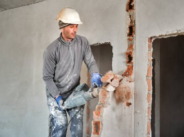 Koruyucu miğferli, pervaneli işçiler odasının içindeki tuğla duvarın yıkımını tamamlıyor. Duvarların ve bölümlerin sökülmesi için tamirat yapan kişi..