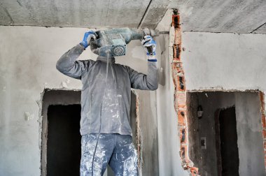 Duvarları yıkmak için özel bir aletle çalışan güçlü bir tamirci. Tuğla bölmesini içeriden sökerken matkapla çalışan işçinin yan görüntüsü.