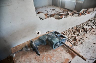 İnşaat ve yıkım için elektrikli çekiç matkabı olan ahşap masa. Yıkıma ve yıkılmış duvarlı evde tadilat için profesyonel bir araç.