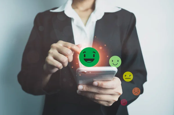 Customer satisfaction concept, client is satisfied with pressing smile face icon by smart phone, excellent service, impressed with care, highest rating and score, good feedback from users.