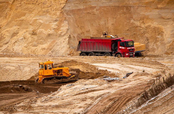 самосвал, грузовик загружен большим количеством песка от развития песчаной карьеры с экскаватором.