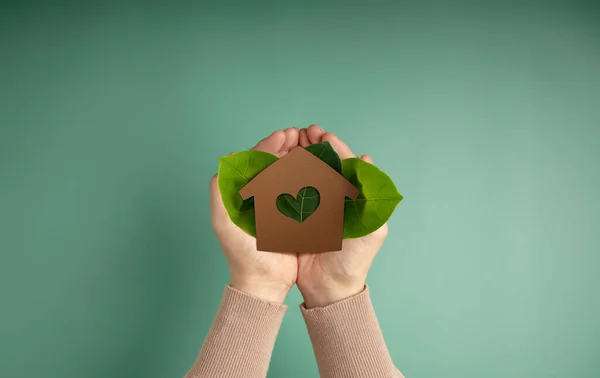 Eco House, Carbon Neutral Concepts. Clean Energy. Green Power. Hands Holding a Craft Papaer House and Green Leaf. Sustainable Resources, Environmental Care. Top View