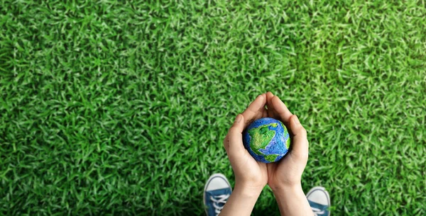 World Earth Day Concept. Green Energy, ESG, Renewable and Sustainable Resources. Environmental and Ecology Care. Hands of Person  Embracing Green Globe in Park. Top View