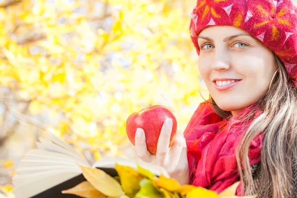 Charmantes Mädchen mit Apfel im Herbstpark und liest Buch — Stockfoto