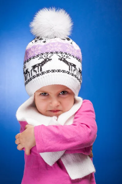 Porträtt av en arg flicka klädd i en stickad rosa och vita vinter mössa. Stockbild