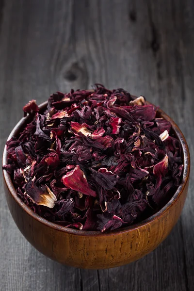 Heap of hibiscus tea in a wooden bowl on old board — Stock Photo, Image
