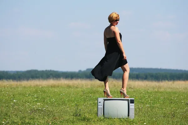 Ragazza con vecchia tv in mezzo ai campi — Foto Stock