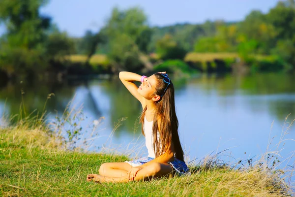 Klein meisje zitten door de rivier de kustlijn in de zomer Stockfoto