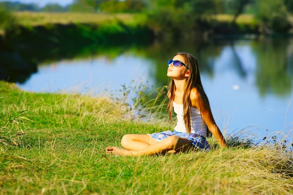 Маленькая девочка, сидящая на берегу реки в летнее время Лицензионные Стоковые Фото