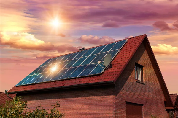 家の赤い屋根の上の太陽電池パネル 太陽が沈む美しい空の写真のコラージュ 代替電源 持続可能な資源の概念 ストック写真