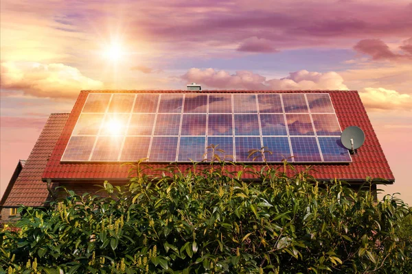家の赤い屋根の上の太陽電池パネル 太陽が沈む美しい空の写真のコラージュ 代替電源 持続可能な資源の概念 ストック画像