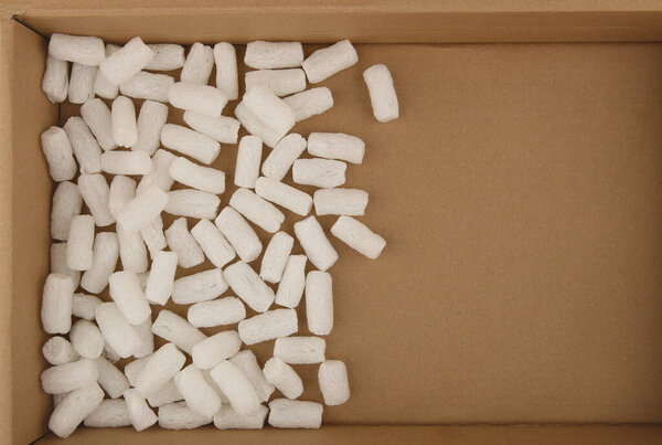Styrofoam packing peanuts in cardboard box background. White plastic foam pellets protective for parcel packing.