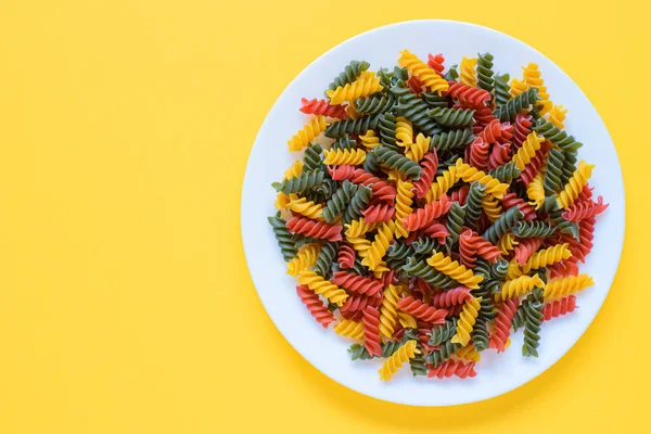 Pasta fusilli cruda secca rossa verde e gialla su un piatto con fondo giallo e spazio per copiare. — Foto Stock