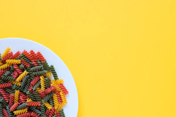 Pasta fusilli cruda secca rossa verde e gialla su un piatto con fondo giallo e spazio per copiare. — Foto Stock