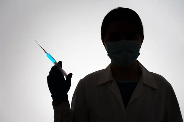 Silhouet van een arts met een spuit gevuld met blauwe vloeistof. Inentingsconcept. Rechtenvrije Stockafbeeldingen