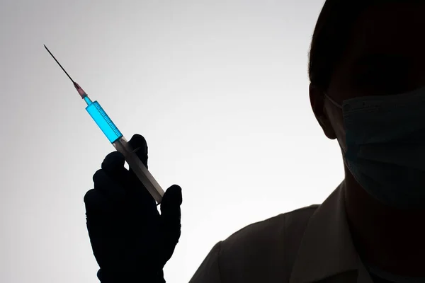 Silueta de un médico con jeringa llena de líquido azul. Concepto de vacunación. —  Fotos de Stock