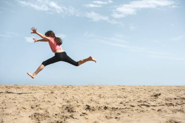 Kumsalda kumda zıplayan mutlu kız.