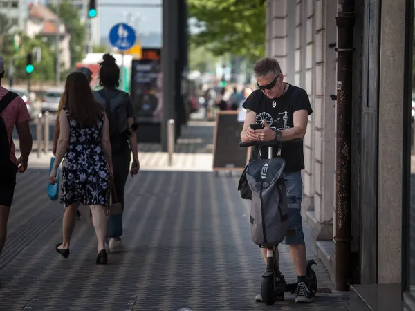 Ljubljana Slovenia 2021年6月16日 若いシニア男性 Ljubljanaの歩行者センターで彼のスマートフォンの携帯電話でインターネットをチェックしながら電動スクーターに乗って — ストック写真