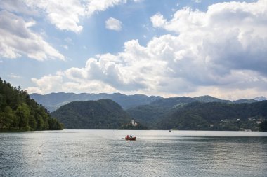 BLED, SLOVENIA - 12 Haziran 2021: Blejsko ostrvo 'nun önündeki bir sandalda turistler, Blejsko Gölü veya Blejsko Jezero adasında, Maria Church, cerkev marijinega vnebovzetja varsayımlarıyla