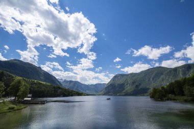 Bohinjsko jezero olarak da bilinen Bohinj Gölü 'nün Panorama' sı, güneşli bir öğleden sonra, denizde bir tekne vızıldıyor. Bohinj Gölü, Slovenya, Avrupa 'daki Julian Alps dağ zincirinin önemli bir simgesidir.