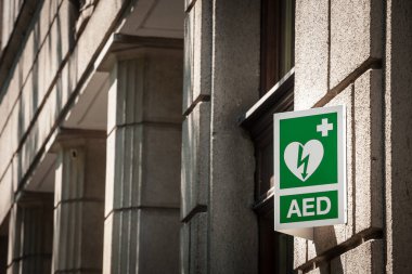 Şehir ortamındaki bir tabelaya elektrik defibrilatörü logosu, Avrupa standartlarına uygun, yakınlarda bir AED cihazı bulunduğuna, kalp hastalıkları ve kalp krizleriyle başa çıkma yükümlülüğü olduğuna işaret ediyor