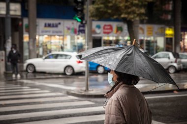 BELGRAD, SERBIA - NOVEMBER 6, 2021: Coronavirus covid 19 sağlık krizi sırasında, Belgrad sokaklarında şemsiyesi altında ağır yağmur altında yürüyen yaşlı bir kadının seçici bulanıklığı