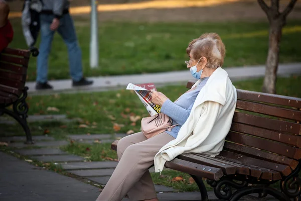 Belgrade Serbia 2021年10月3日 コロナウイルスCovid 19危機の際に顔マスク保護装置を身に着けているベオグラードの路上で新聞を座って読んでいる老婦人の選択的なぼやけ — ストック写真