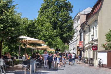LJUBLJANA, SLOVENIA - 15 Haziran 2021: Bir grup çocuk, Ljubljana şehir merkezinin nehir kıyısında, sosyal mesafeye saygı göstermeden, kalabalık bir kafe restoranı avlusundan geçiyor.