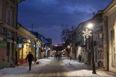PANCEVO, SERBIA - 23 Ocak 2021: Banat bölgesinde kış karlı bir gecede, Pancevo, Njegoseva Ulica 'nın ana caddesinde karda yürüyen insanlar hakkında seçici bulanıklık